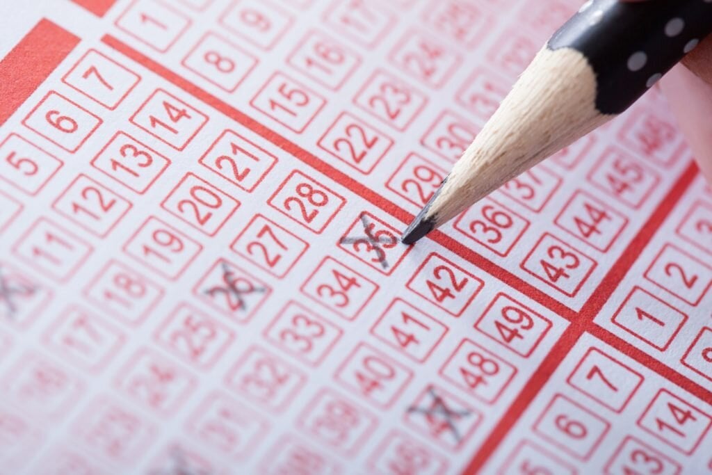 A slip form for a lottery is depicted, with several numbers crossed out using a pencil.